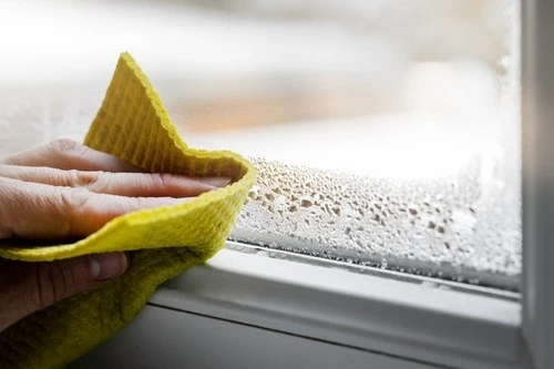 Hand using a cloth to wipe away condensation inside window