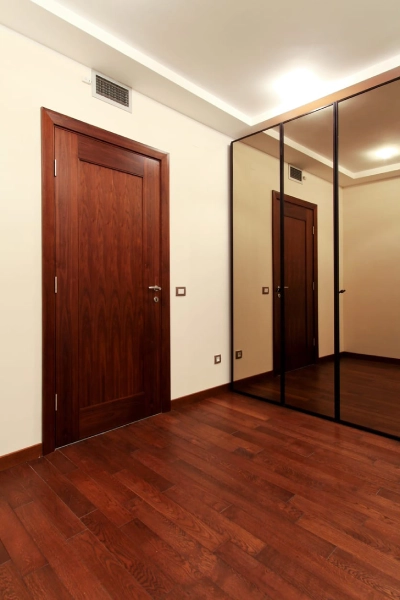 A room featuring polished wooden floors and a large wall mirror reflecting the space.