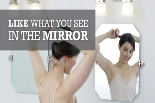 A woman stands before a mirror, observing her reflection.