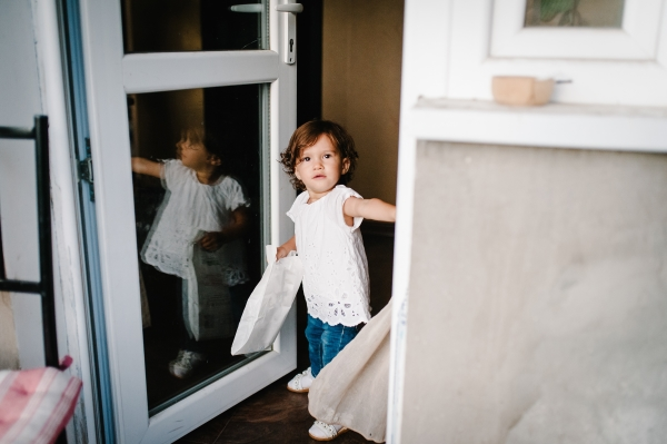 Small child standing next to an open glass door.
