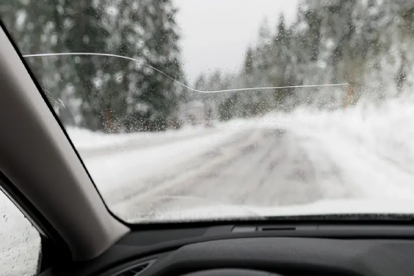 A car with a cracked windshield drives down a snowy road.
