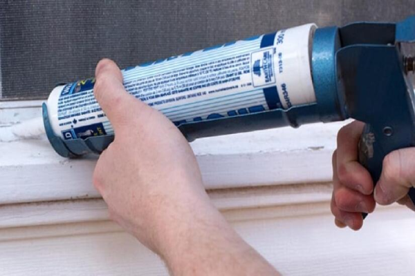 A man sealing a window with caulk.