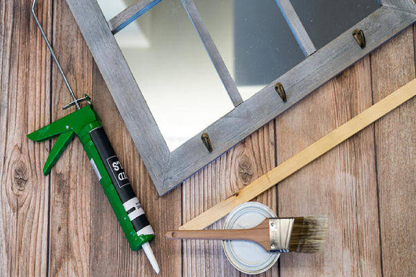 A mirror, paintbrush, and glue gun arranged on a wooden table, showcasing crafting tools for creative projects.