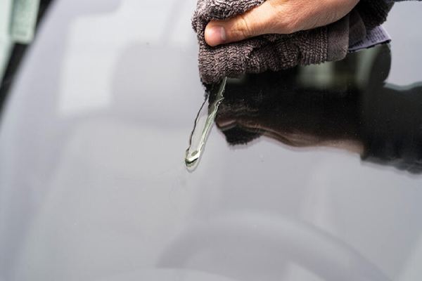 A person cleaning the windshield of a car with a cloth.
