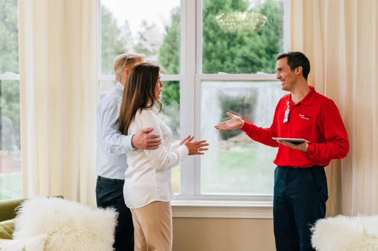 A woman, man, and male Glass Doctor service professional standing in residential living room next to a foggy window.