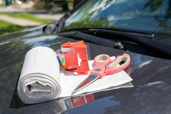 A pair of scissors and a roll of paper placed on the hood of a car, suggesting a crafting or repair activity.