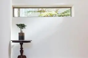 a horizontal shaped window installed into a white wall and a plant and table in front of it