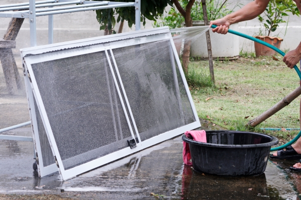 Man using a garden hose, soap, and water to clean window screens