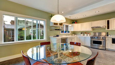 View of dining table with glass top and modern chairs in a kitchen with white storage cabinets.