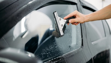 A person wiping a auto glass with a handheld tool.
